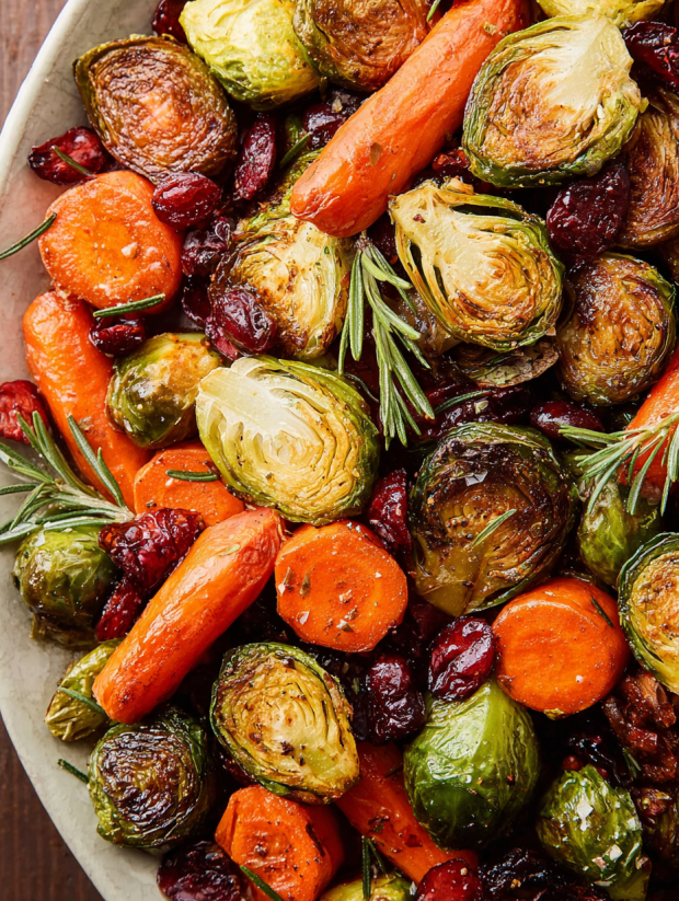 A bowl of roasted vegetables including carrots, brussels sprouts, and red onions.
