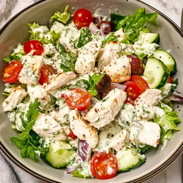 A bowl of salad with chicken, tomatoes, cucumbers, and lettuce.