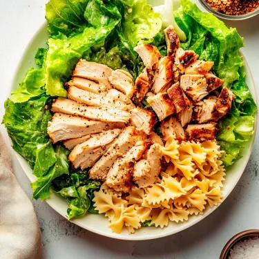 A plate of chicken, pasta and lettuce.