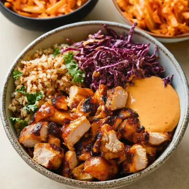 A bowl of food with chicken, rice, and vegetables.