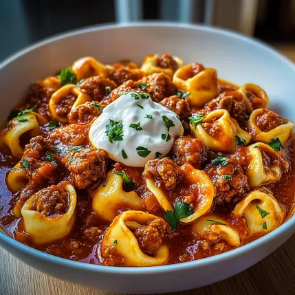 A bowl of pasta with meatballs and a dollop of sour cream.