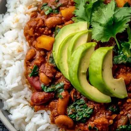 A bowl of chili with rice and avocado.