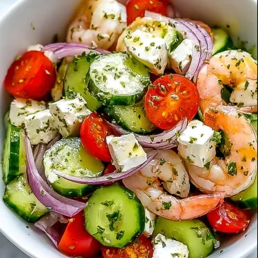 A bowl of shrimp salad with tomatoes, cucumbers, and feta cheese.