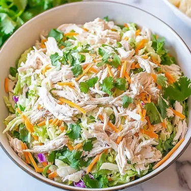 A bowl of chicken salad with carrots and lettuce.