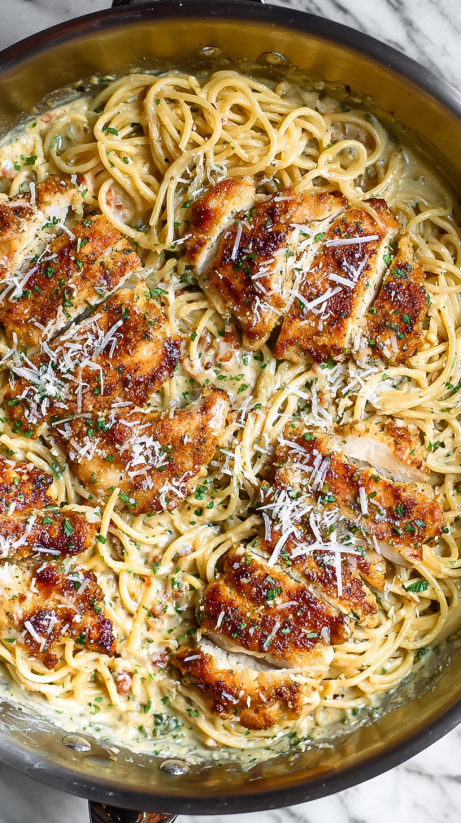 A dish of chicken and pasta with cheese and herbs.