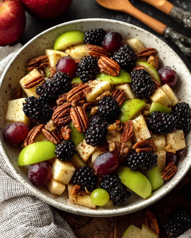 A bowl of fruit salad with apples, grapes, and blackberries.